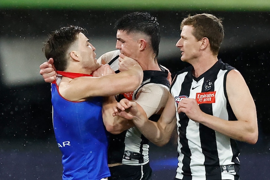 Two AFL players come together in a melee, showing anger with each other.