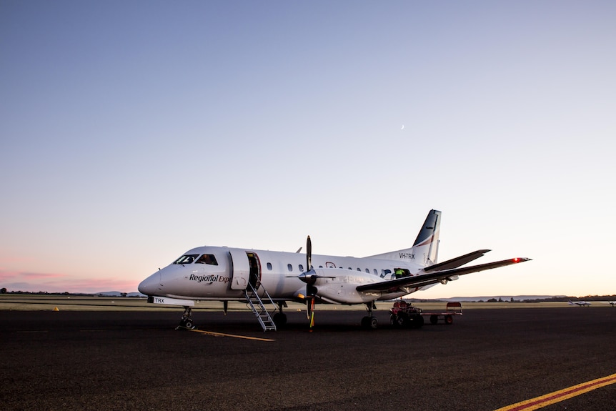 propeller airplane with REX logo sits on tarmac at dusk.