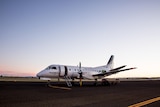 propeller airplane with REX logo sits on tarmac at dusk.