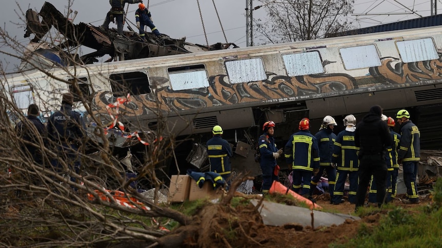Rescue workers stand near a mangled train carriage at the crash site. 