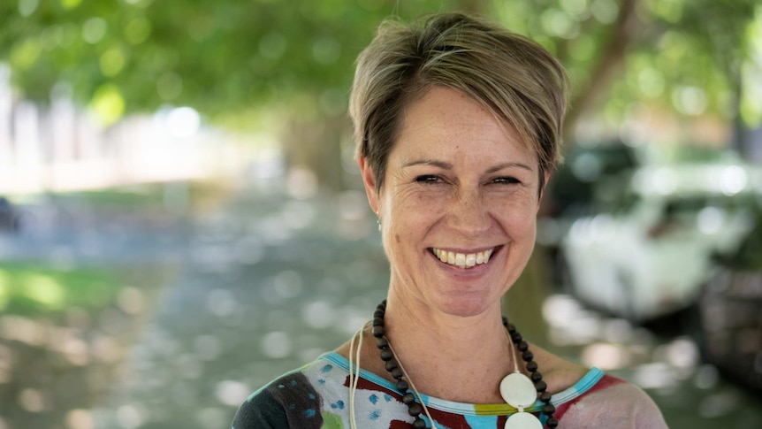 Headshot of smiling woman on footpath under trees.