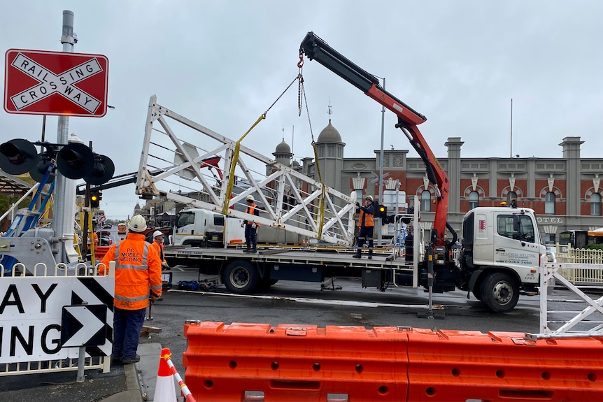 Construction workers lift historic railway crossing gate out of it's place with a crane. 