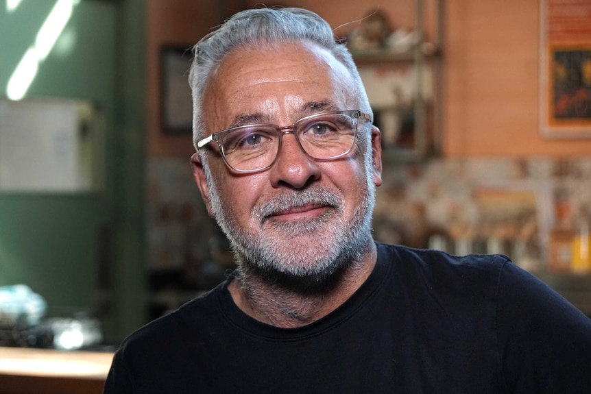 A close up of a man wearing reading glasses and a black t-shirt.