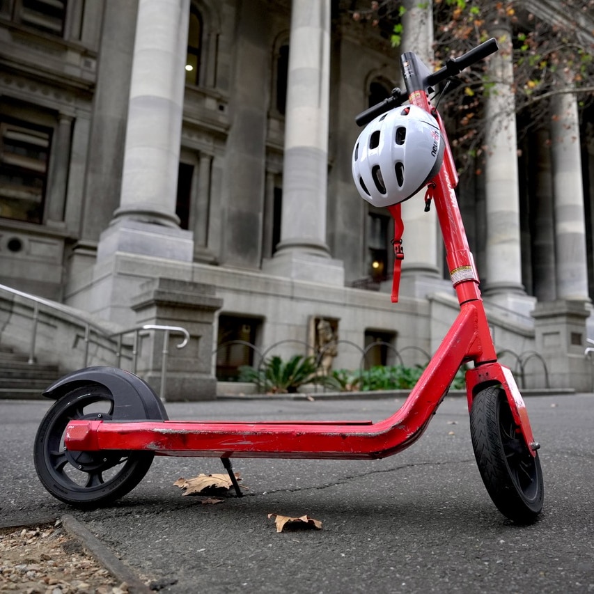 An e-scooter stands on a footpath.