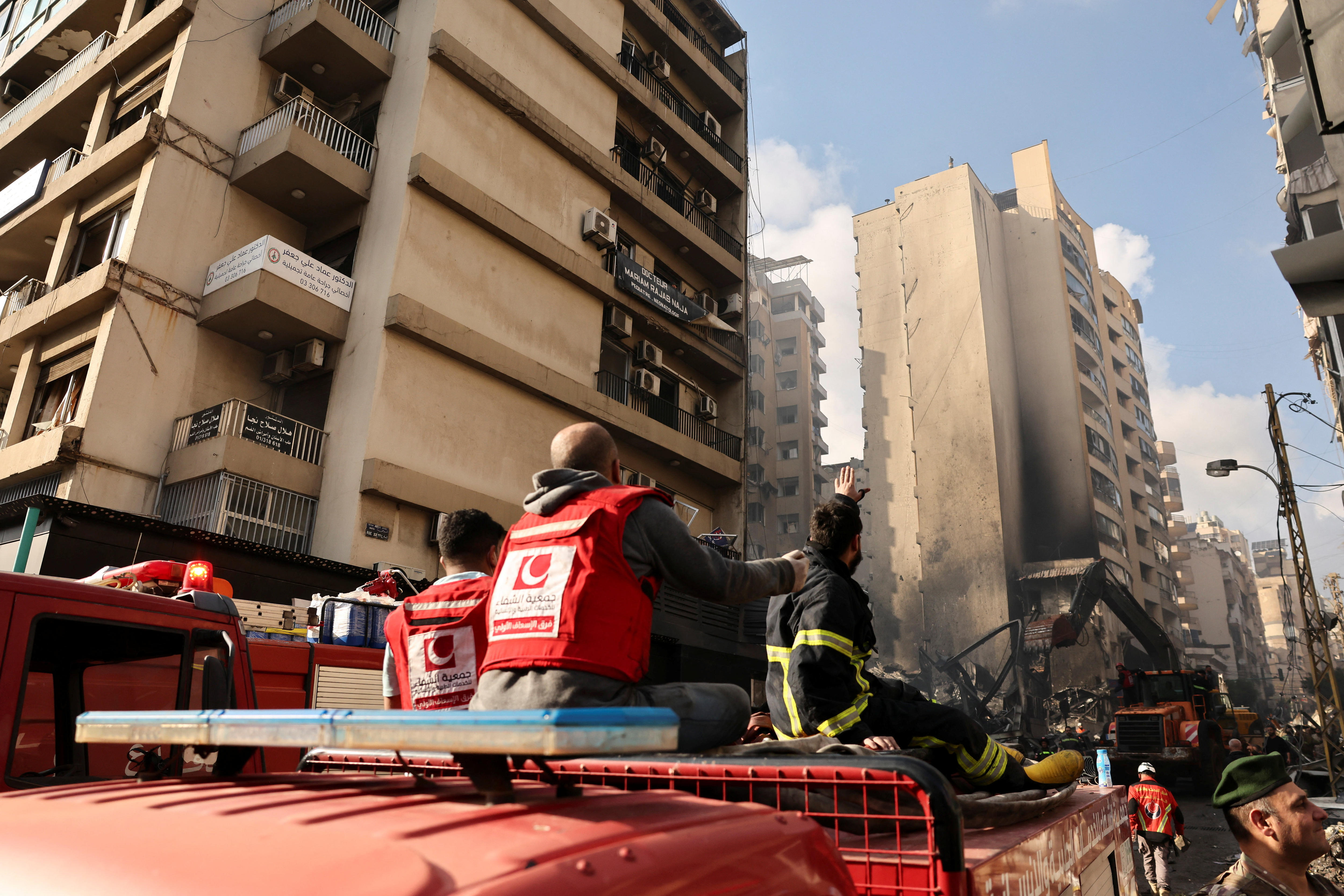 Emergency workers sitting on top of a truck parked by tall apartment towers partially destroyed by an air strike.