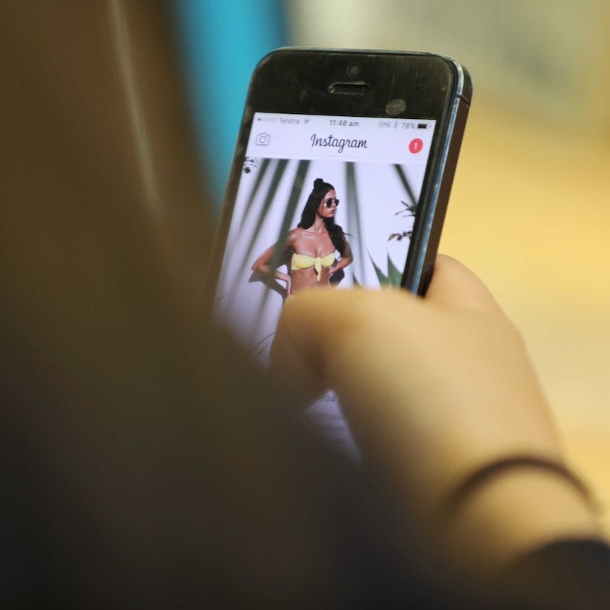 A teenage girl looks at a bikini model on Instagram on her phone.