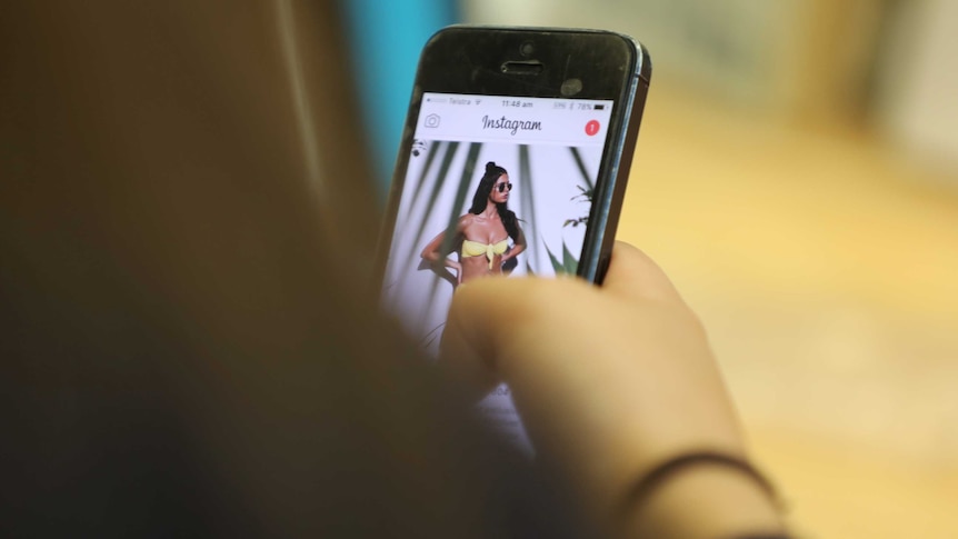 A teenage girl looks at a bikini model on Instagram on her phone.