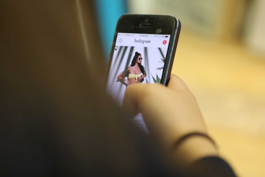 A teenage girl looks at a bikini model on Instagram on her phone.