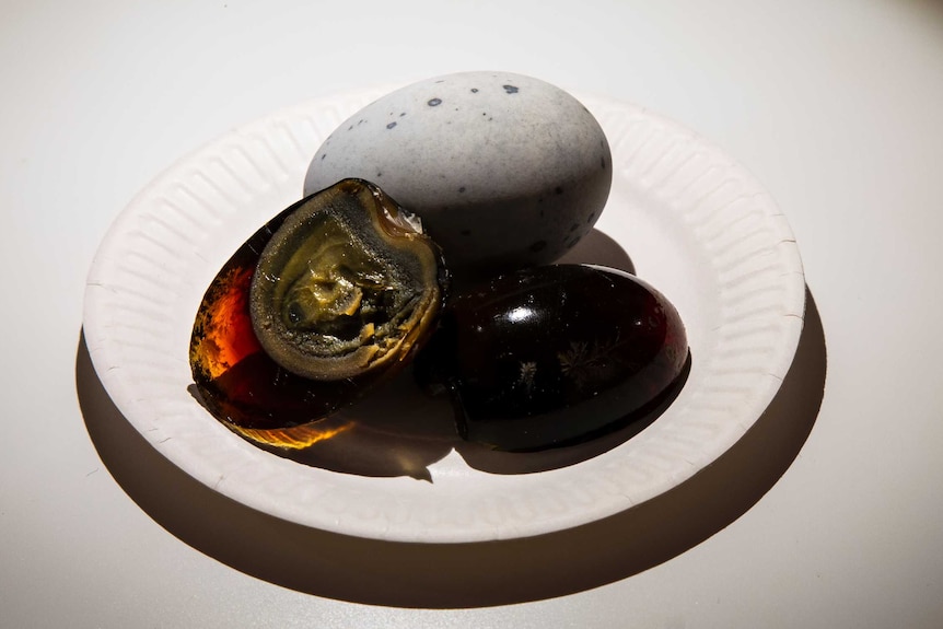 A plate of century eggs, including one in its shell, one without its shell and one that has been cut in half.