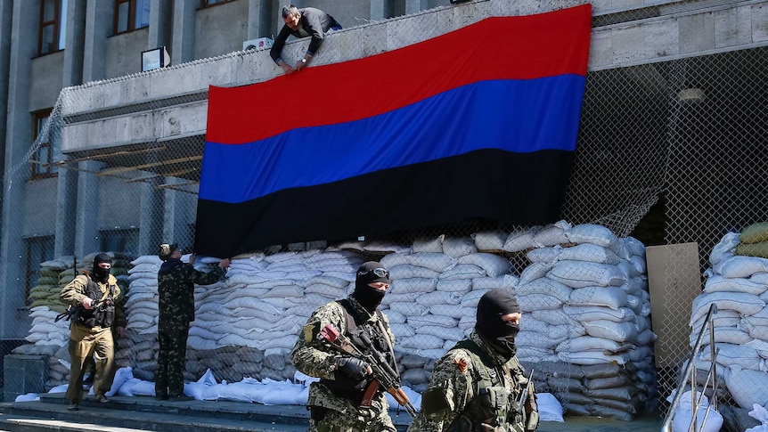 Armed pro-Russian men walk past activists hanging a Donetsk Republic flag in Slaviansk, Ukraine.