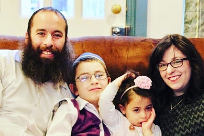 Photograph of a young Jewish family, beared father, two young  children and wife on a couch, smiling at camera