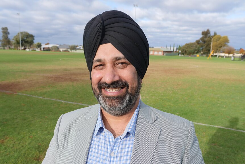 A man wearing a turban standing on a sports field and smiling