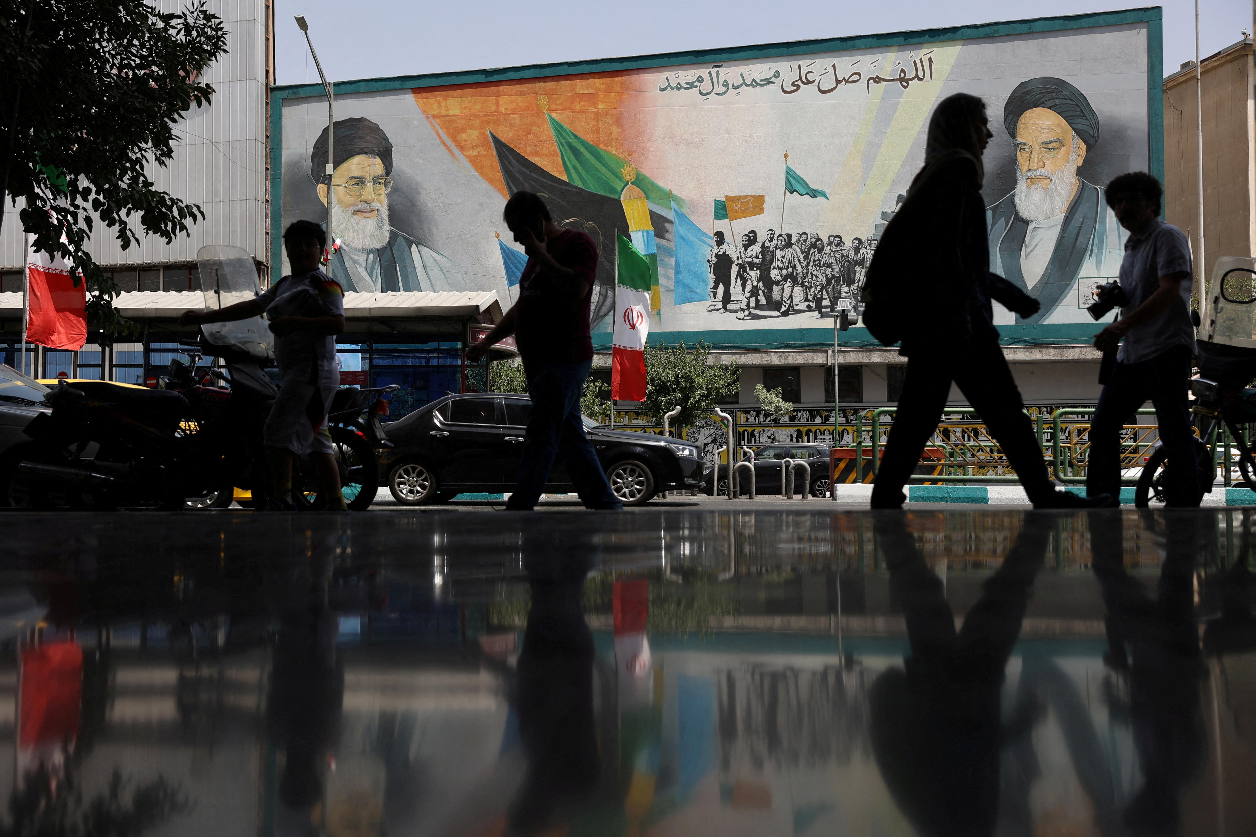Pedestrians walk in Tehran in front of billboard with Surpeme Leader Ali Khamenei