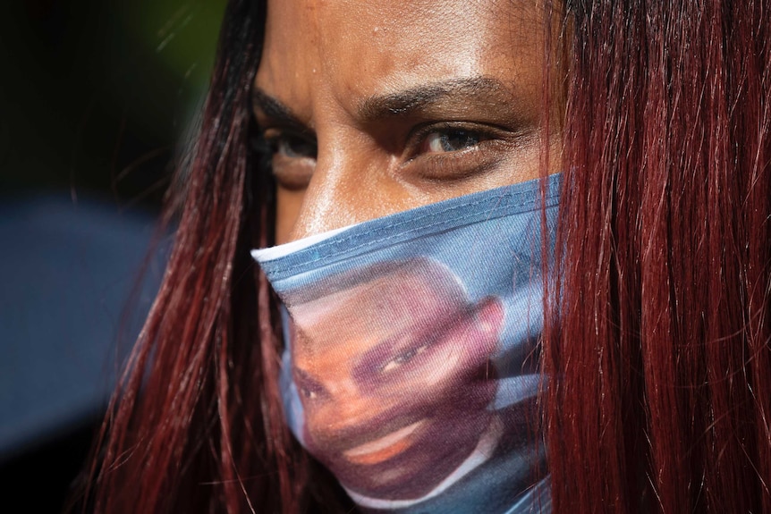 A woman wears a face covering with the likeness of shooting victim Ahmaud Arbery printed on it.