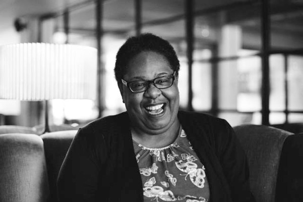 A woman wearing glasses laughs in a black and white photo.