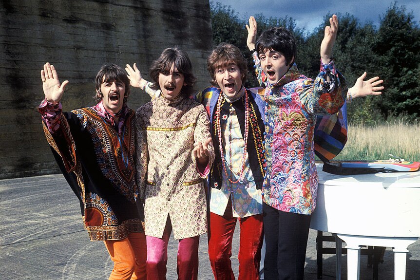 Ringo Starr, George Harrison, John Lennon and Paul McCartney wear colourful outfits and wave their hands in the air.