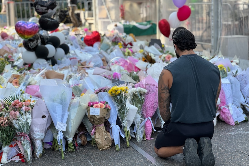 A man sitting looking at flowers in a tribute at Bondi Junction shopping centre.