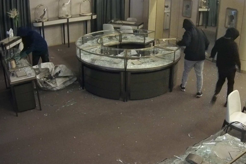 three hooded people in a jewellery store with its display cases smashed