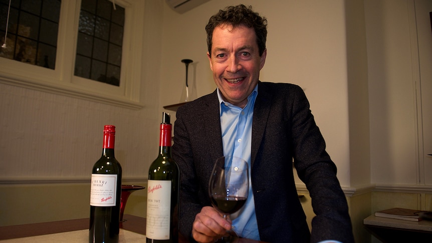Peter Gago sits smiling at table with two bottles of Penfolds wine.