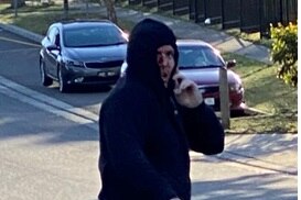 A man in a black hoodie looks at the camera as he appears to hold a mobile phone up to his ear.