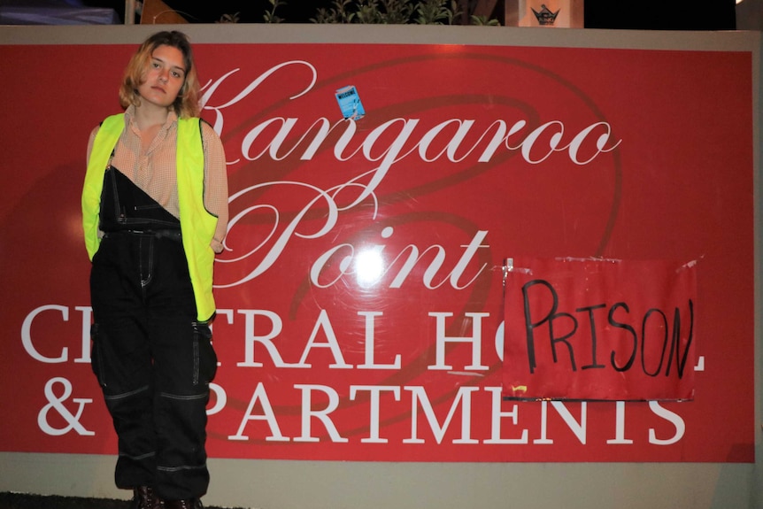 Activist Zoë Hulme-Peak stands in front of the modified hotel sign that says "prison"