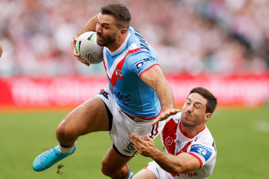 A Sydney Roosters NRL player holds the ball as he is tackled by a St George Illawarra opponent.