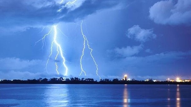 Lightning can be seen in a blue sky, reaching from clouds to the Darwin skyline.