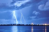 Lightning can be seen in a blue sky, reaching from clouds to the Darwin skyline.