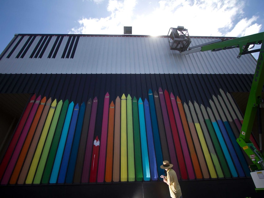 Artwork on outside of building depicts colourful pencils down below and piano keys up top. Several stories high.