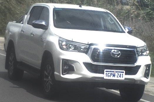 A white Toyota Hilux driving on a road.
