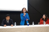 三位候选人中讲台上，中间一位女士站立讲话。
