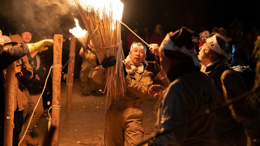 A Japanese man carries a huge bundle of flaming torches.