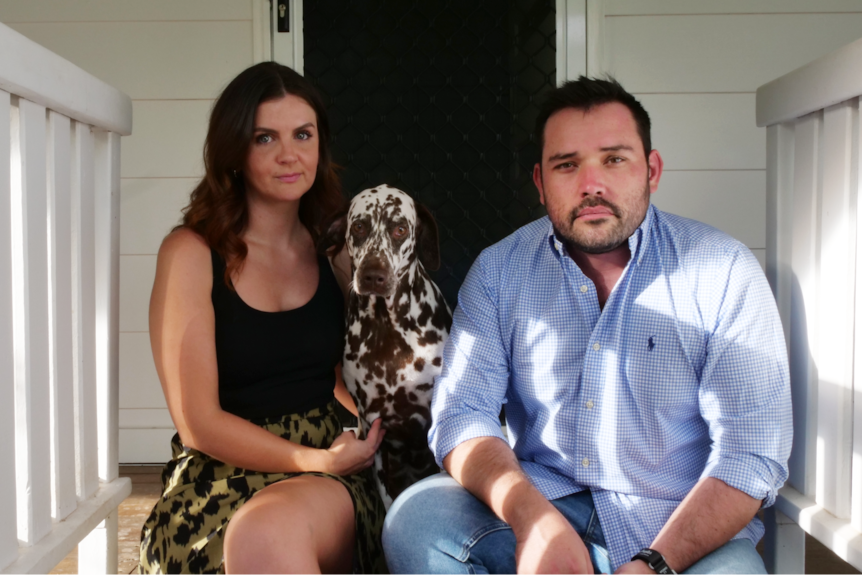 A white couple sitting on the steps to their front door with a dalmation. 