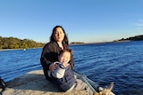 picture of a woman and a child sitting on a rock by the beach