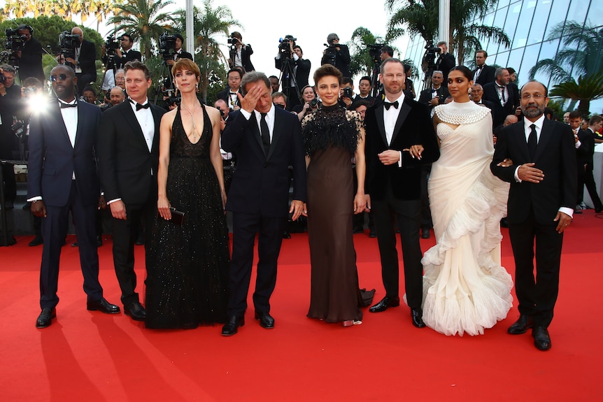 Eight people line up on the red carpet in formal suits