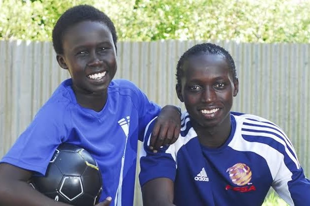 Two teenage boys with black skin wearing blue soccer jerseys pose for a photo
