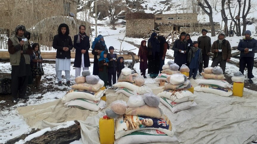 A group of people stand in the snow near food relief packages.