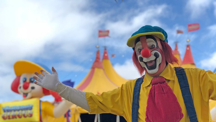 A clown stands outside a circus tent