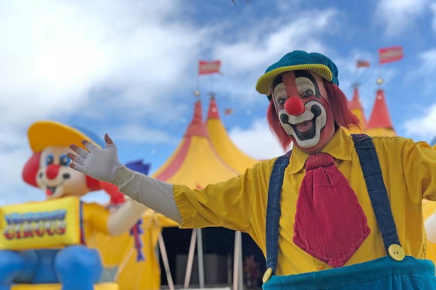 A clown stands outside a circus tent