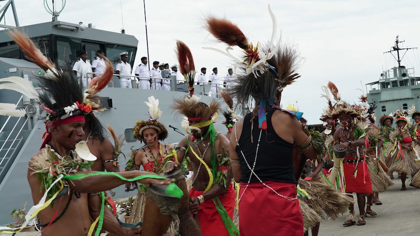 Papua New Guineans in traditional dress dance in front of a naval patrol boat