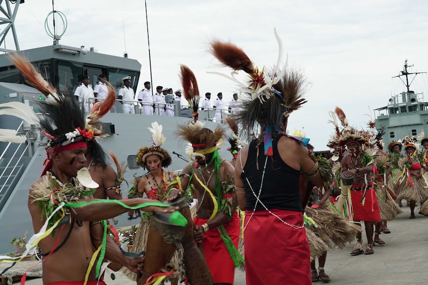 Papua New Guineans in traditional dress dance in front of a naval patrol boat