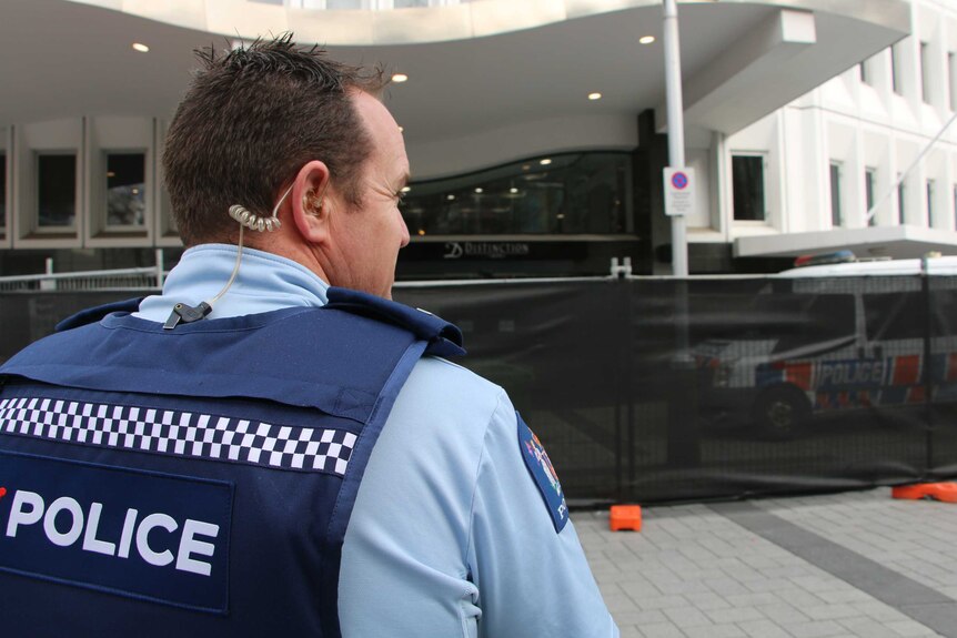 NZ police officer stands in front of fenced hotel driveway