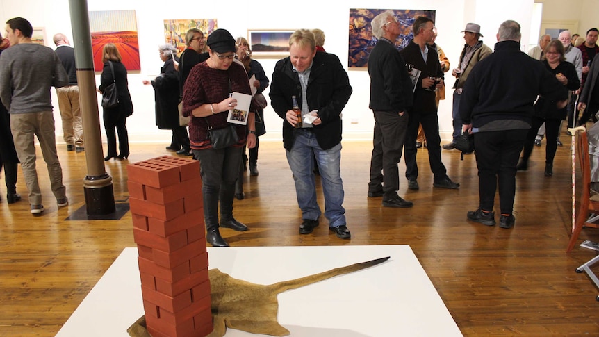 The artwork 'Footprint', depicting a pile of red bricks on top of a kangaroo skin, all of which is carved from wood.