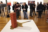 The artwork 'Footprint', depicting a pile of red bricks on top of a kangaroo skin, all of which is carved from wood.
