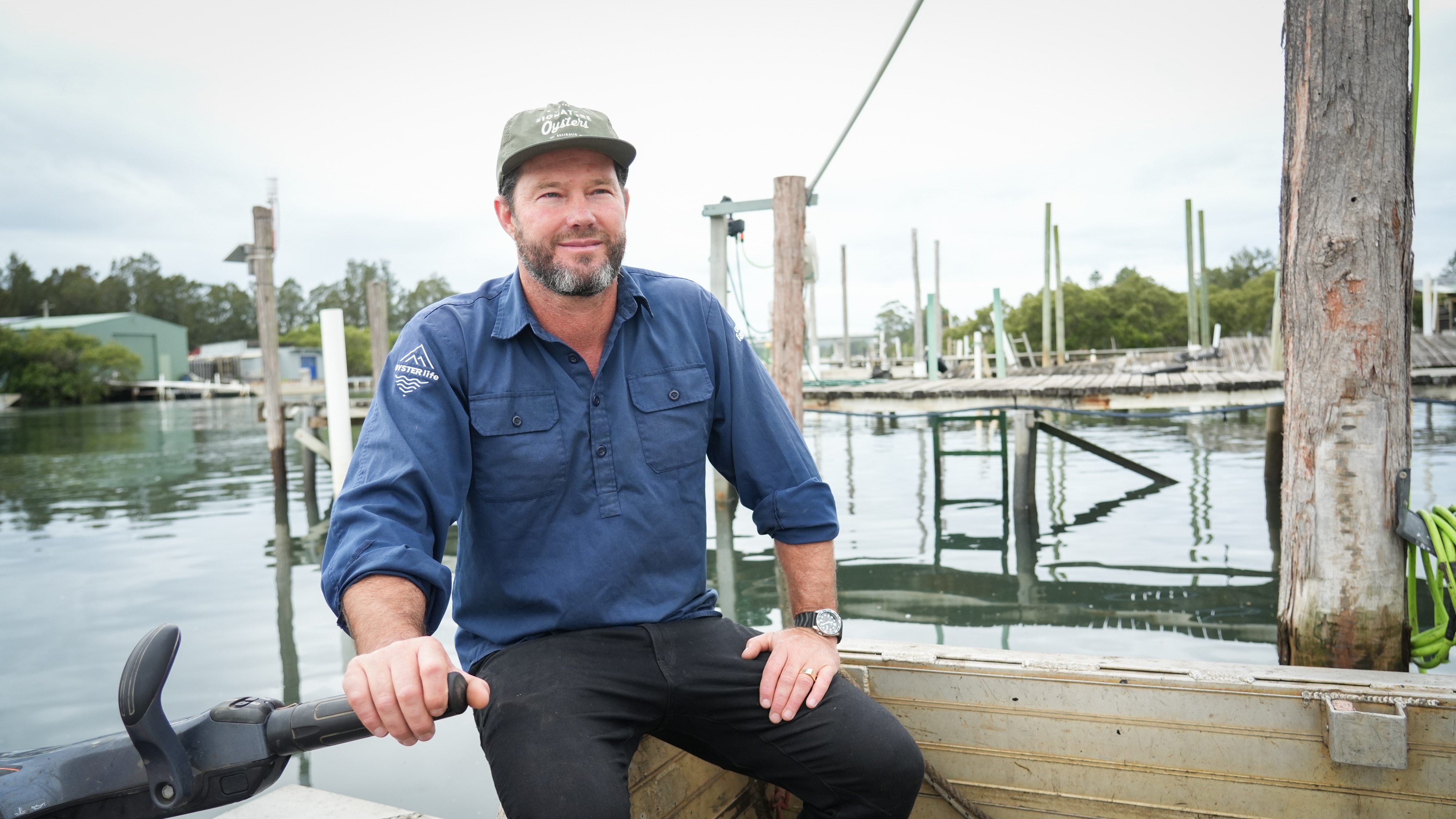 A man on a boat with a marina behind him.