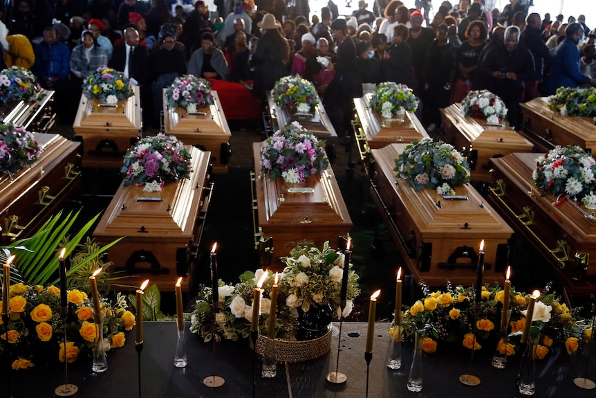 Rows of caskets are laid out before mourners at a group funeral for the victims of the nightclub poisoning. 