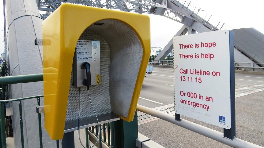 Emergency phone and sign for suicide helplines at walkway entry to a bridge in Brisbane