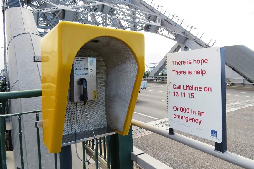 Emergency phone and sign for suicide helplines at walkway entry to a bridge in Brisbane