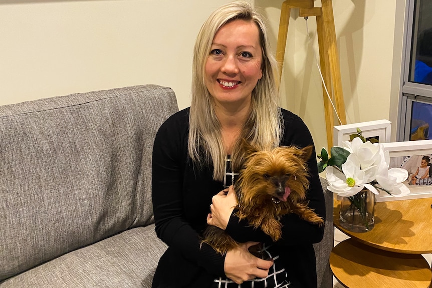 Woman holds small brown and black terrier with silky fur on a couch