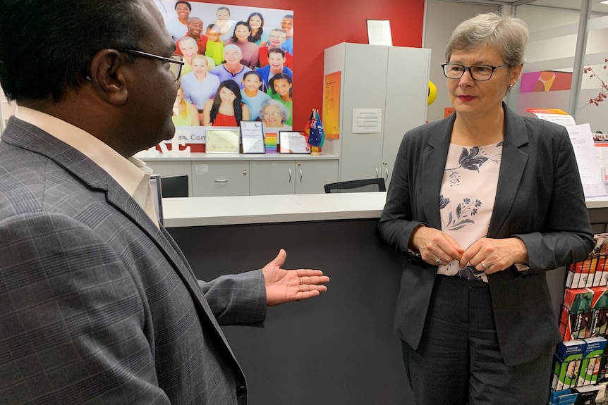 Elizabeth Drozd speaking to a man in an office, that has a photo of a group of smiling people hanging on the wall.